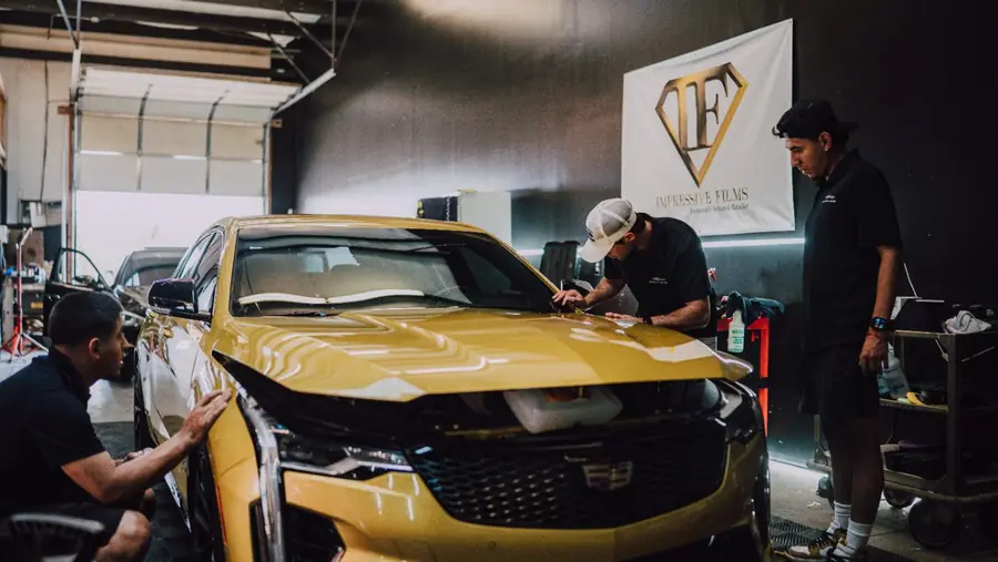 Three Evo Solutions technicians working on the hood of a gold Cadillac CT4-V